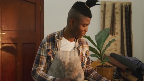 African-american-craftsman-in-checked-shirt-and-apron-smiling-in-leather-workshop