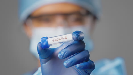 close up of female lab research worker wearing ppe holding test tube labelled vaccine