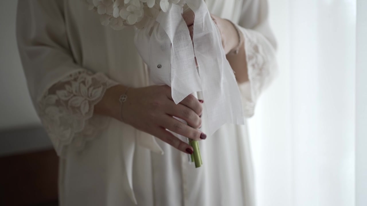 Close view of bride hands holding bouquet with ribbon and lace robe