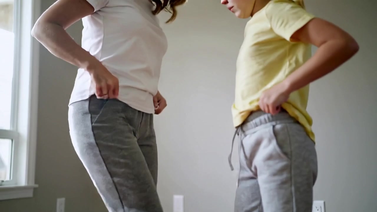 After brief hug mother and daughter adjusting waists while checking fit at home, with window light