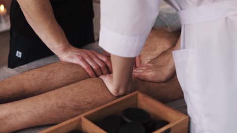 close-up,-female-and-male-massage-therapists'-hands-perform-a-four-hand-massage-on-sportsmen's-legs