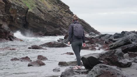 Woman-close-to-the-waters-edge-near-a-rocky-shore-in-Ponta-Delgada,-Azores,-Portugal