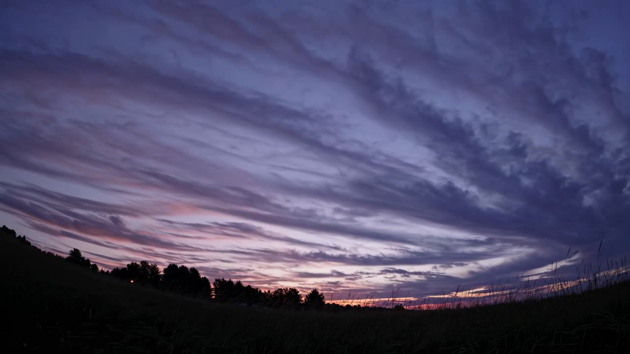 A wide-angle video captures a serene sunset over a grassy field, with dramatic clouds painted