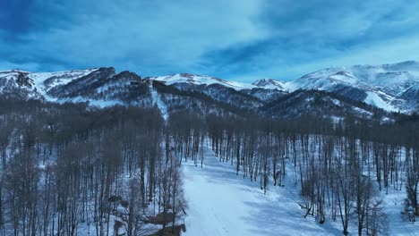 Una-Vista-Aérea-De-Un-Pueblo-De-Montaña-Nevado,-Con-Calles-Y-Edificios-Cubiertos-De-Nieve-Entre-Los-Picos