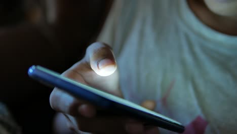 Teenage-boy-sitting-on-sofa-using-smart-phone-at-night