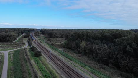 dutch train passing on a railway track on a summer day in the netherlands, drone shot