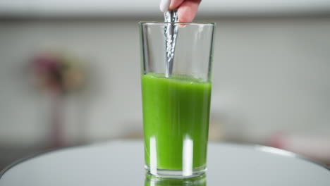 index finger gently pressing on surface of fresh green vegetable juice in a clear glass