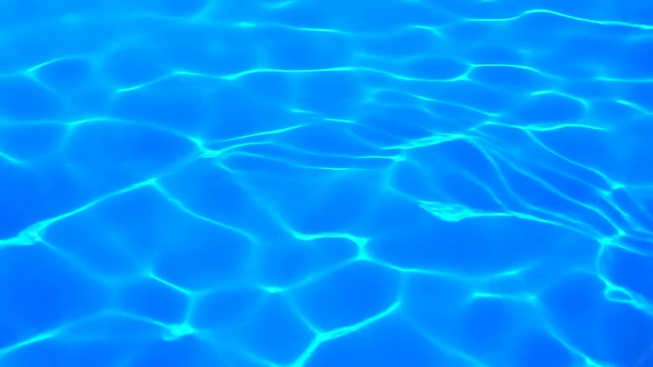 Air kolam biru cerah memenuhi bingkai dengan riak lembut, pantulan yang bergeser, dan pola permukaan abstrak yang bersih di bawah sinar matahari yang hangat