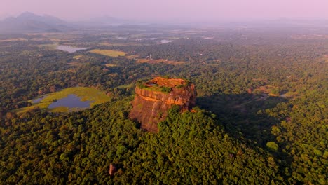 a stunning aerial clip of sigiriya rock at sunrise, surrounded by lush jungle and a serene lake reflecting the morning light.