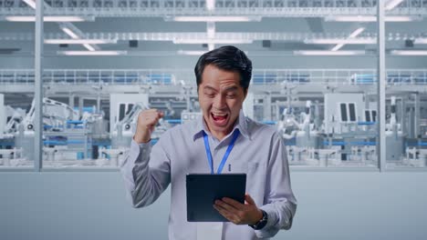 asian male professional worker standing with his tablet at factory digitalization, he raises his fist up with screaming goal