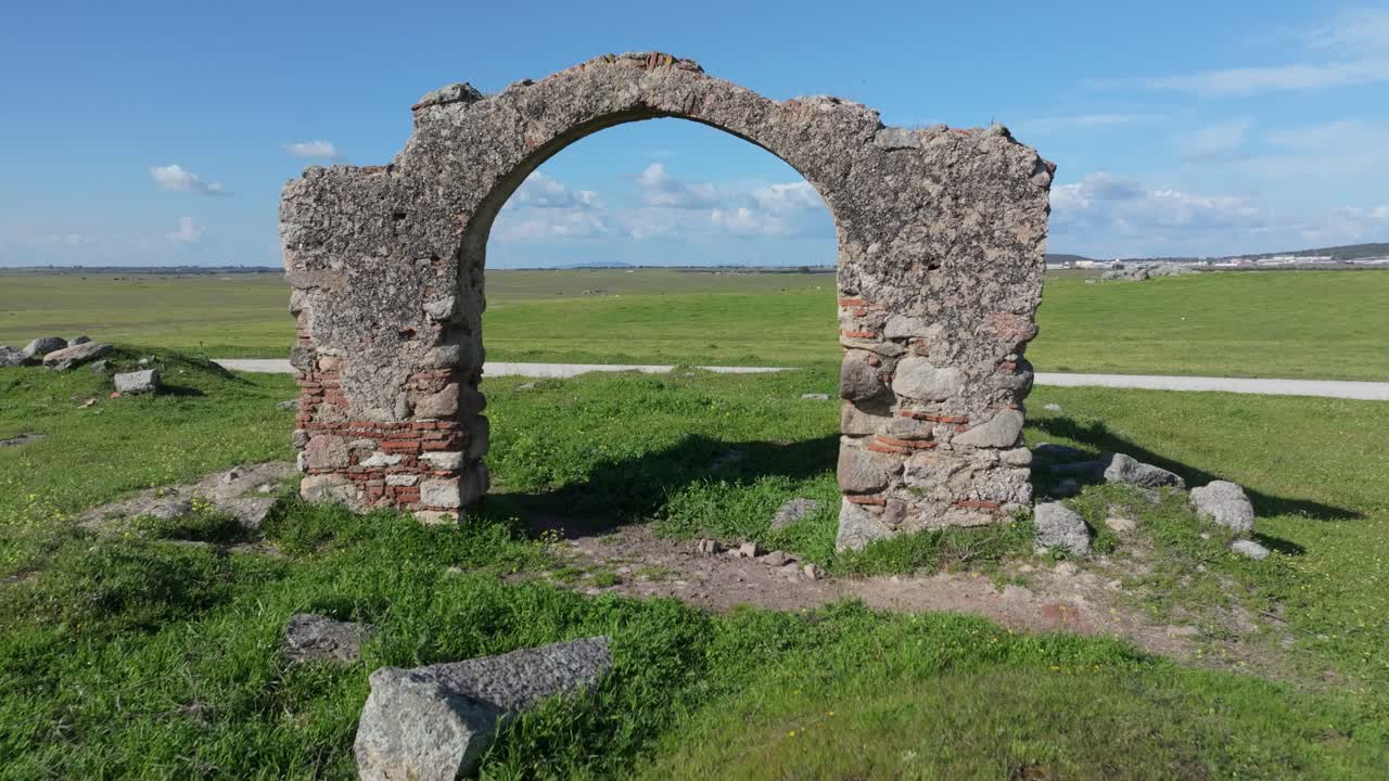 Reverse drone shot in a green pasture showing the stone and brick archway known as “Puerta de Arenas.” The drone passes through the arch, creating a surprise effect from inside the ruins.