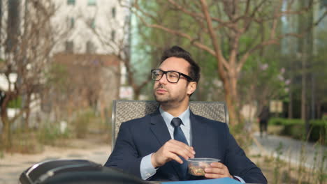 pensive millennial businessman eating nuts in park outdoors enjoying lunch break