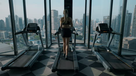 Woman Running on Treadmill in a High-Rise Gym with City View