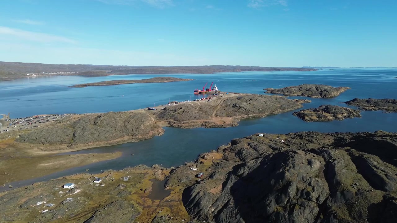 Tasainen eteenpäin suuntautuva ilmasta kuvattu drone-kuva, joka seuraa keinotekoista aallonmurtajapengertä kohti telakoitua rahtilaivaa Iqaluitin syväsatamassa