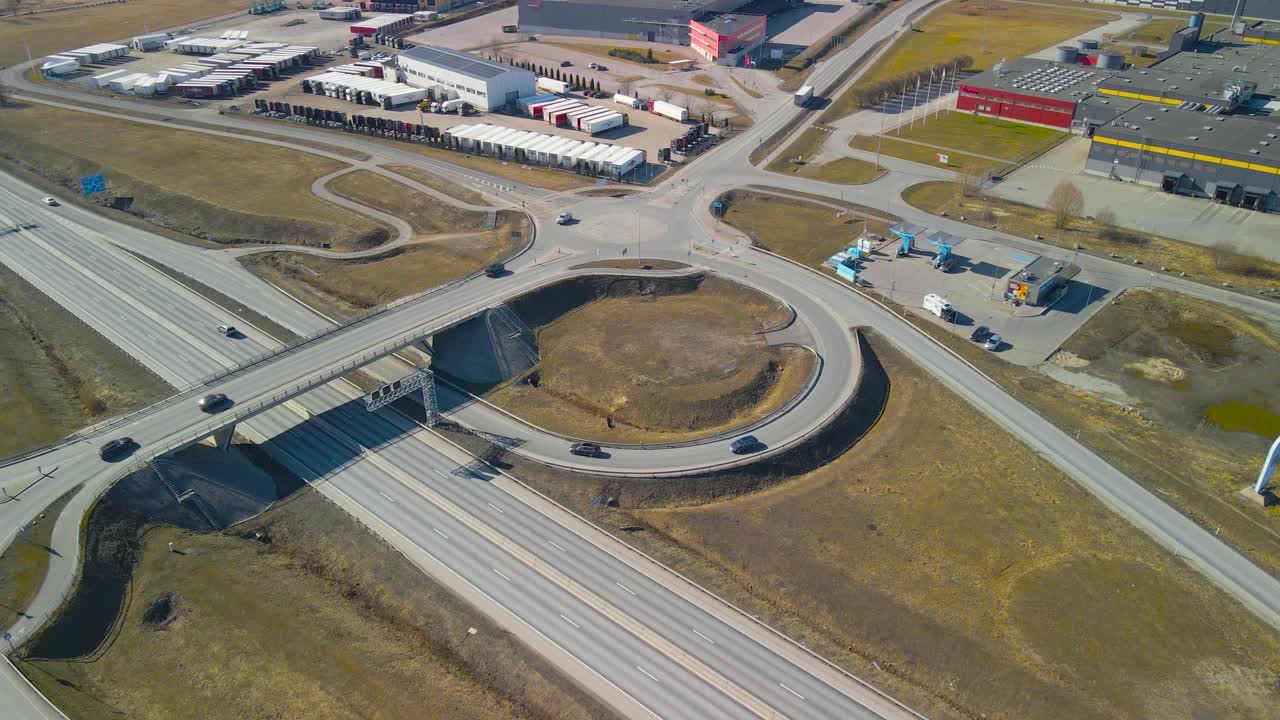 Aerial drone footage of a busy intersenction with bridges and roundabouts in Jüri Estonia during a spring sunny day while cars, vehicles and trucks are driving on the roads and below the bridge.