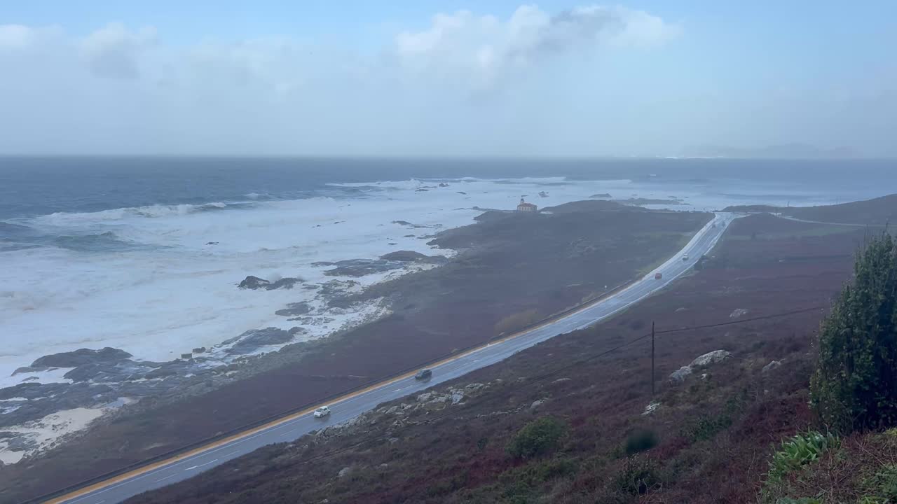 Carros circulando por uma estrada com o mar agitado ao fundo na Galiza