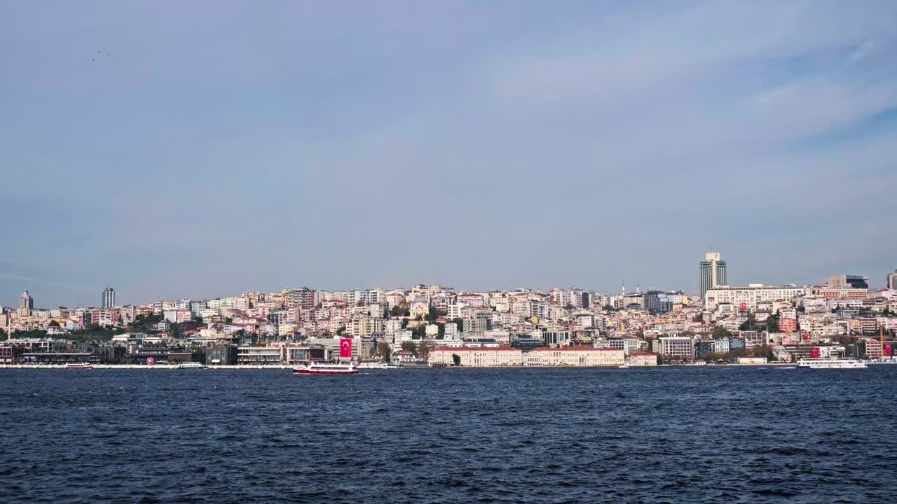 A scenic seascape of Istanbul's historic Sarayburnu point. A ferry crosses the water with the ancient walls of Topkapi Palace and lush trees in the background