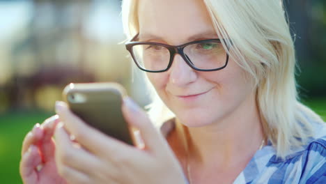 portrait of a young woman wearing glasses enjoying a smartphone in the park beautiful sun glare 4k s