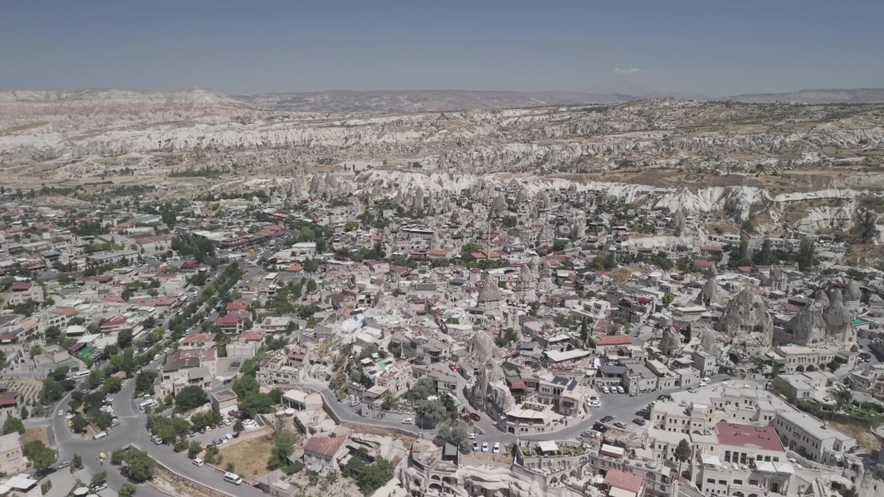 Ripresa con drone 4K a 10 bit in avanti e in salita sopra l'iconico centro città di Goreme in Cappadocia, Turchia. Filmato panoramico di una soleggiata giornata estiva di splendidi edifici tradizionali in pietra e formazioni rocciose