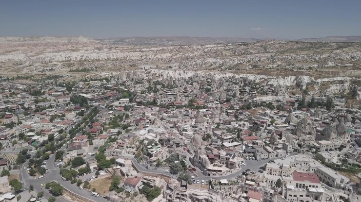 Ripresa con drone 4K a 10 bit in avanti e in salita sopra l'iconico centro città di Goreme in Cappadocia, Turchia. Filmato panoramico di una soleggiata giornata estiva di splendidi edifici tradizionali in pietra e formazioni rocciose