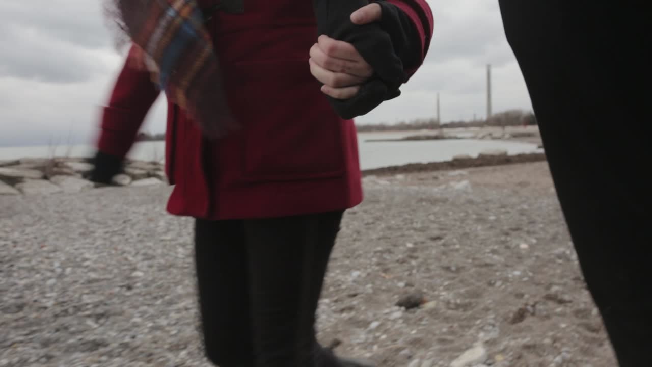 Tourist Couple Wearing Jacket Walking Along The Rocky Shore While Holding Hands - Medium Shot