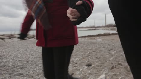 tourist couple wearing jacket walking along the rocky shore while holding hands - medium shot