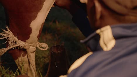 Close-up-of-a-young-Ugandan-native-milking-an-Ankole-watusi-cow-at-night-in-Uganda,-Africa