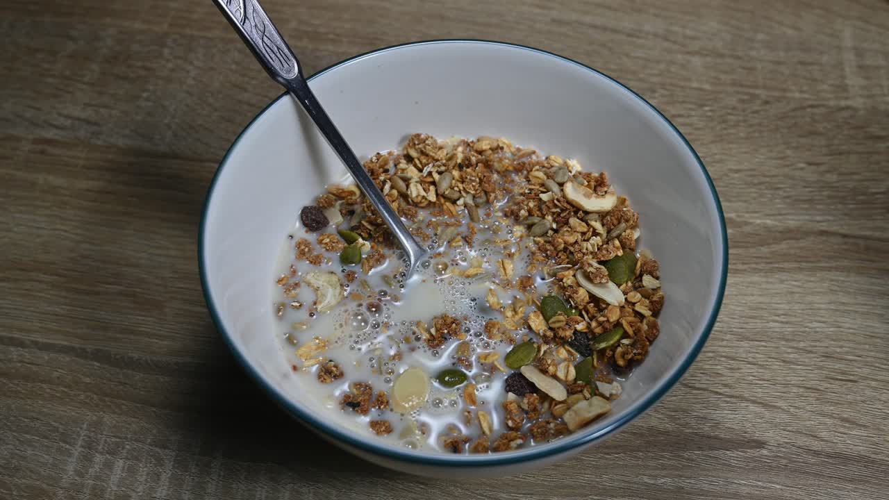 granola en un bol con una cuchara y leche de almendras recién vertida haciendo burbujas, semillas, frutos secos, desayuno saludable