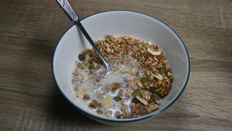 granola en un bol con una cuchara y leche de almendras recién vertida haciendo burbujas, semillas, frutos secos, desayuno saludable