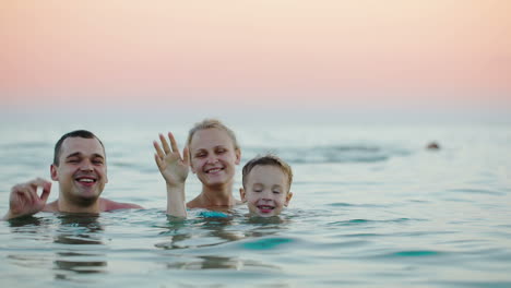 Dreiköpfige-Familie-Winkt-Mit-Den-Händen-Vom-Meer-Aus