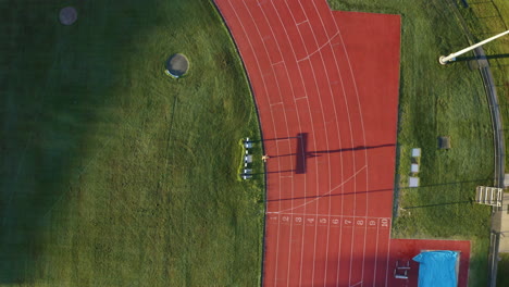 aerial 4k drone view of fit athlete running fast laps on outdoor red race track