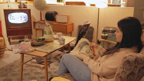 Woman-Sitting-On-The-Couch-While-Reading-Old-Magazine-Inside-The-Nostalgia-Museum-In-Motola,-Sweden