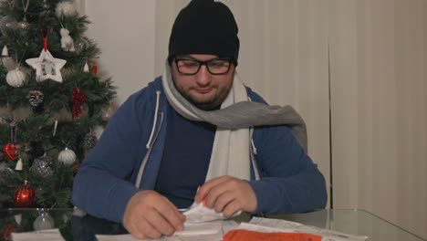 hombre frío con sombrero y anteojos frustrado, molesto con un montón de recibos financieros en navidad