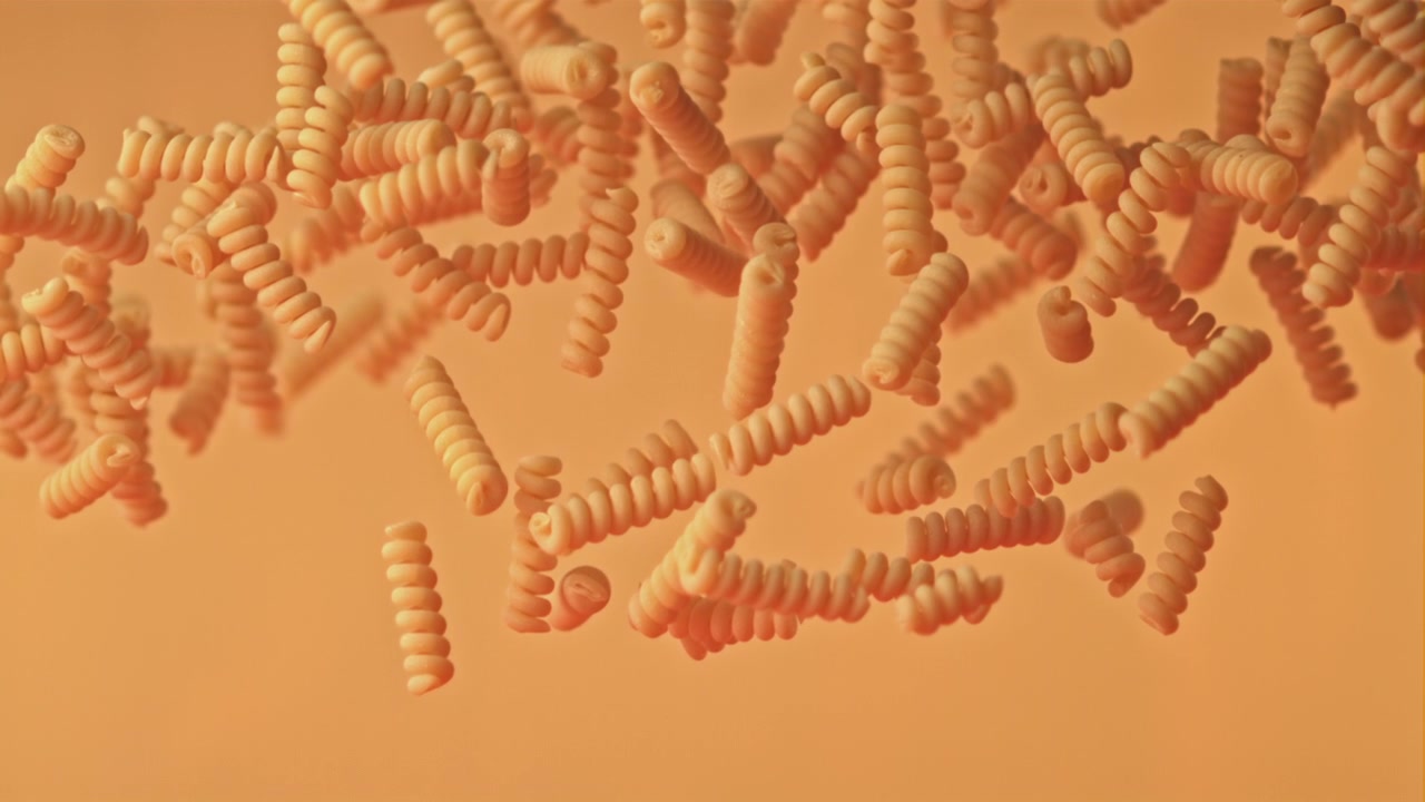 Uncooked Fusilli Pasta Floating in Slow Motion on an Orange Background