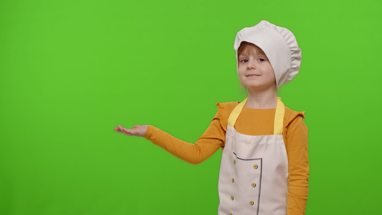 Bambina vestita da chef che indica a sinistra su uno spazio vuoto, spazio per il tuo logo pubblicitario