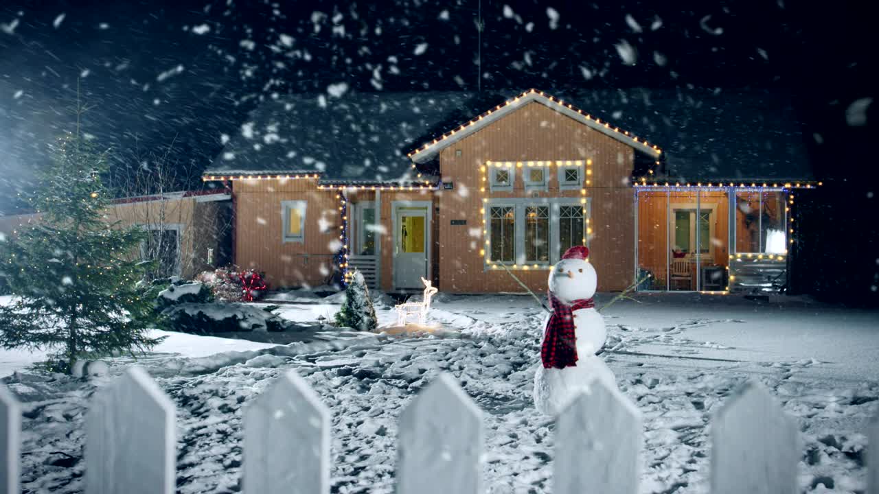 Footage of the Idyllic House Decorated with Garlands on Christmas Eve, Snowman and Christmas Tree stand on the Front Yard. Beautiful Winter Evening with Falling Soft Snow.