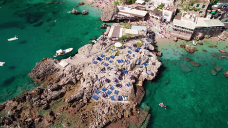 An-epic-aerial-shot-rotating-around-a-rocky-beach-and-sparkling-blue-water-in-Marina-Piccola-on-Capri,-a-famous-island-that-is-a-popular-luxury-vacation-destination-in-Italy-along-the-Amalfi-Coast