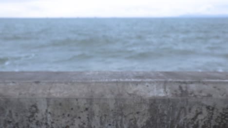 camera pulls back over wall as violet waves come in frame to crash on large rocks