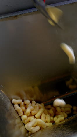 sweet snacks made of maize are dropped into metal can. manufacturing of vegetarian snacks at enterprise. close up. vertical video