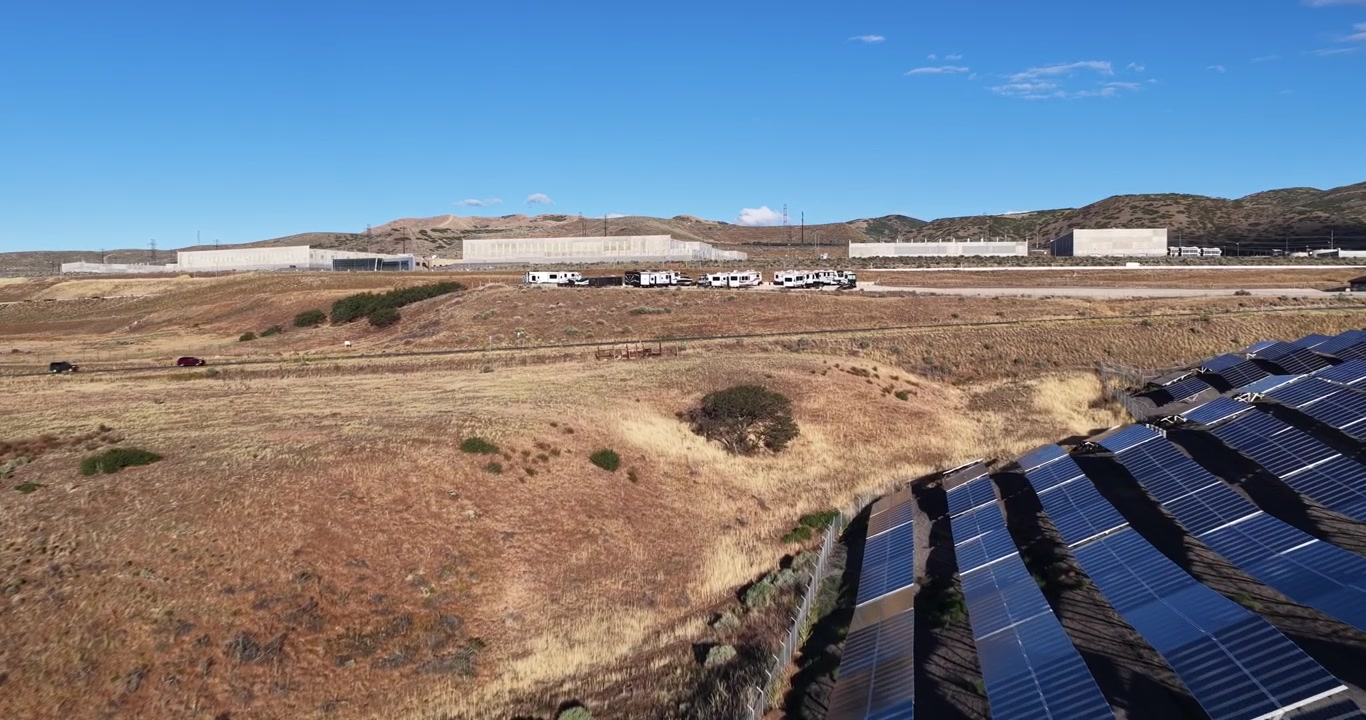 Skinnende solcellefelter og tørt Utah-landskab mod det vidtstrakte NSA Utah Datacenter på en solrig dag, der viser integrationen af vedvarende energi.
