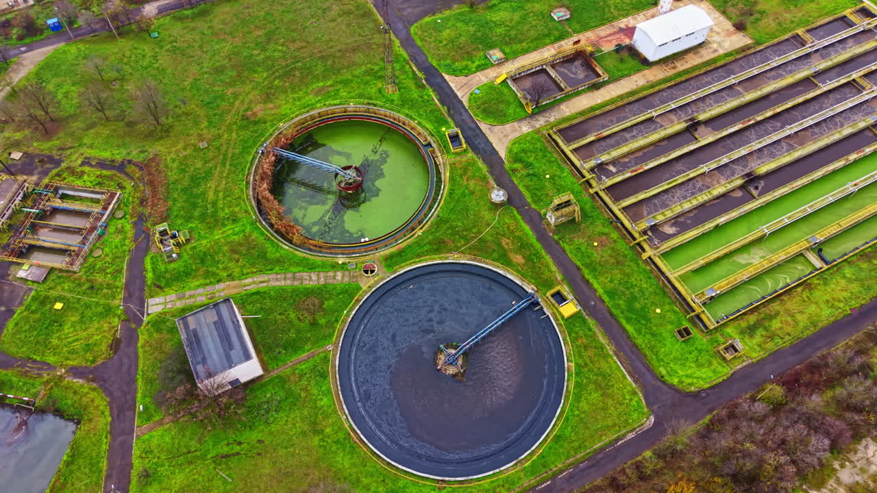 View of water treatment facility with different tanks and green surroundings during daylight in an outdoor setting