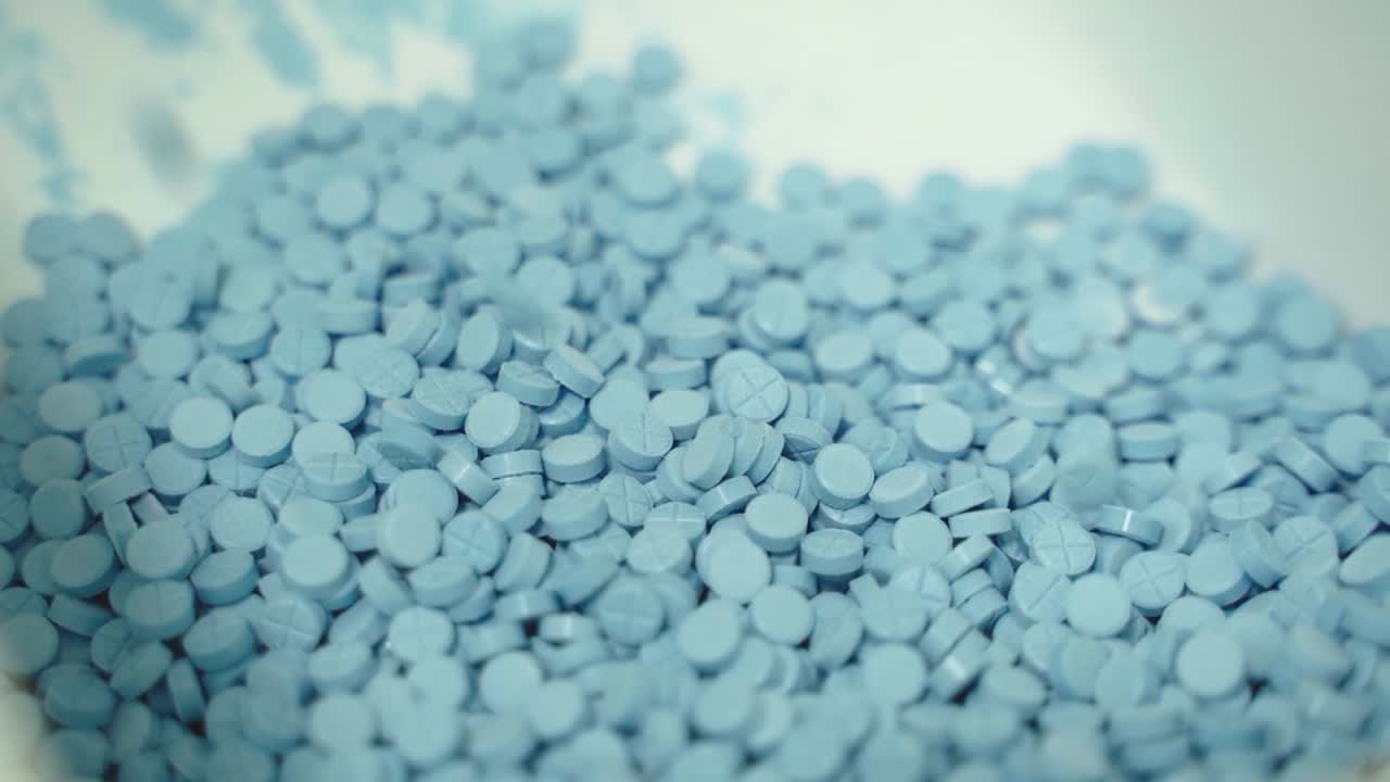 Pile of blue pharmaceutical tablets in bulk storage are ready for packaging.