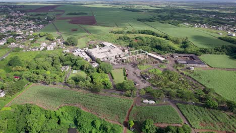 a sugar factory in mauritius surrounded by green fields and residential areas, daylight, aerial view