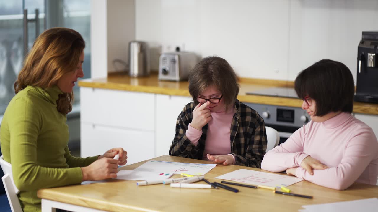 Due ragazze con disabilità disegnano in cucina accanto all'insegnante o alla madre.