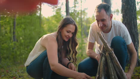 a couple man and a woman together collect a fire from sticks in the woods. a young couple in a hike puts a fire for the night and cooking in nature