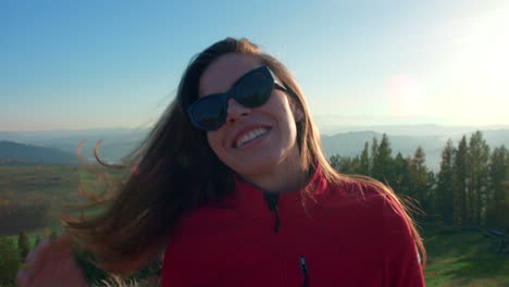 happy girl smiles standing in sunglasses at a top of the hill with amazing outdoor landscape in the background