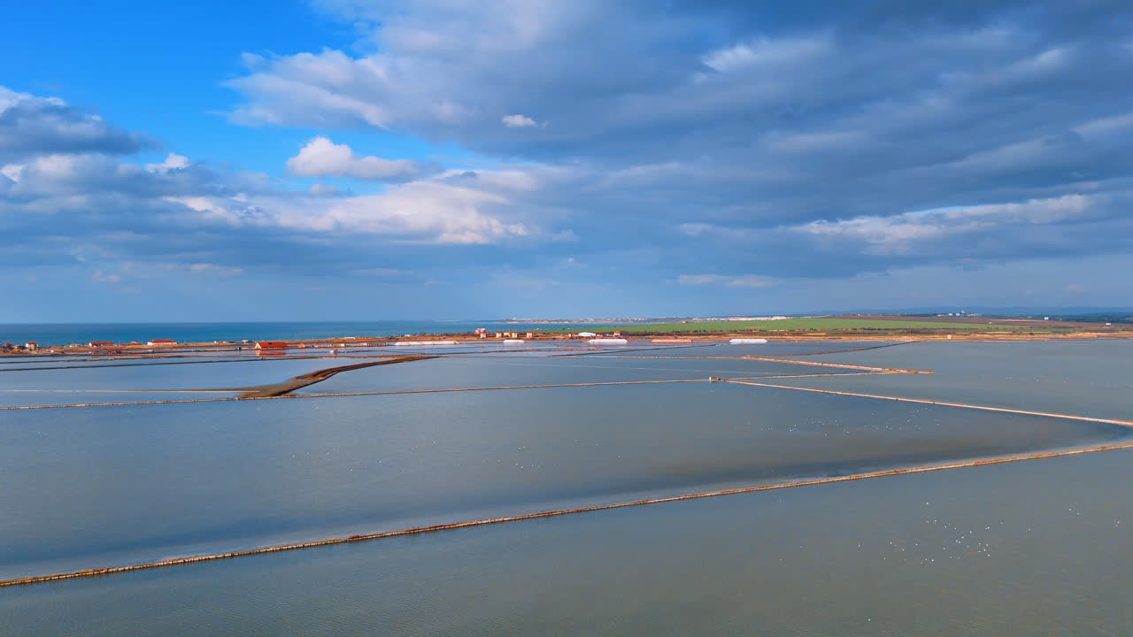 Panoramaudsigt over et saltudvindingsanlæg nær havet. Et højt vinkelperspektiv, der viser omfanget af saltbassiner, der grænser op til kystlinjen.