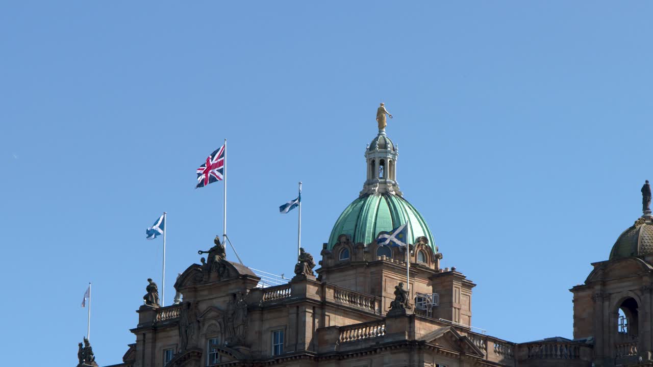 Daytime upward pan of ornate classical building dome with waving flags against clear blue sky
