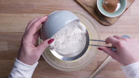 female baker straining flour to the beaten eggs for carrot cake preparation - high angle shot