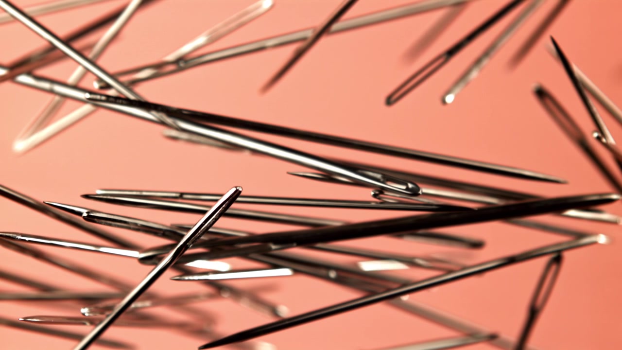 Metallic Sewing Needles Coming into Focus on a Peach Background